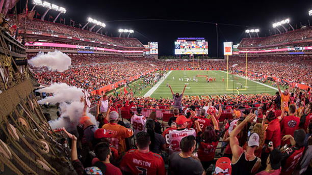 Wide stadium shot of fans, dressed in red cheering on Tampa Bay Buccaneers