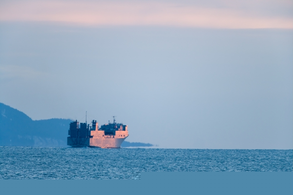 Photograph of a military ship on dark blue water, during a sunrise, exiting Kachemak Bay in Alaska