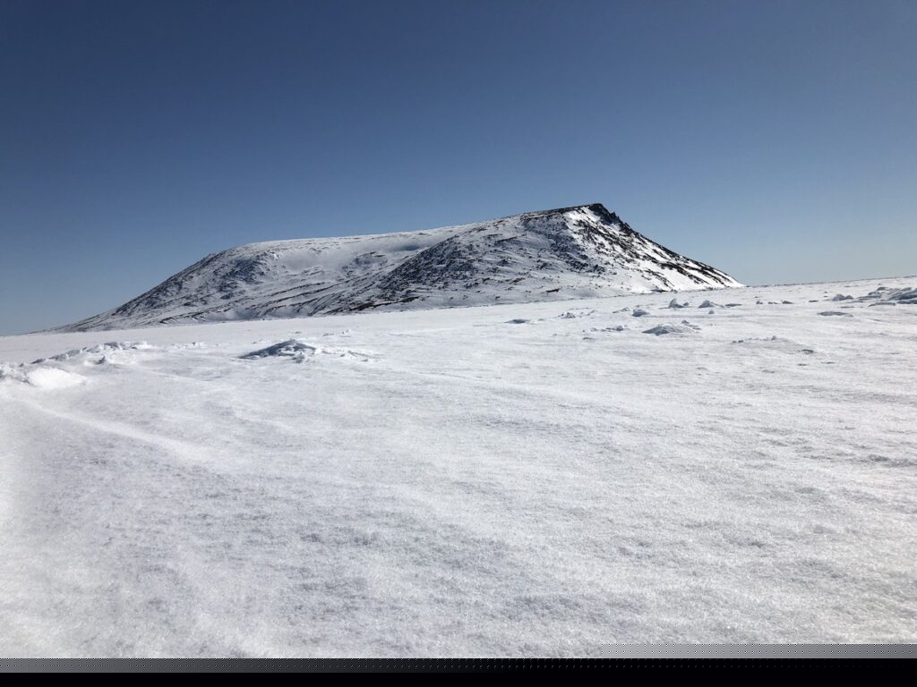 A snowy white landscape with a snow covered hill against a clear, blue sky.