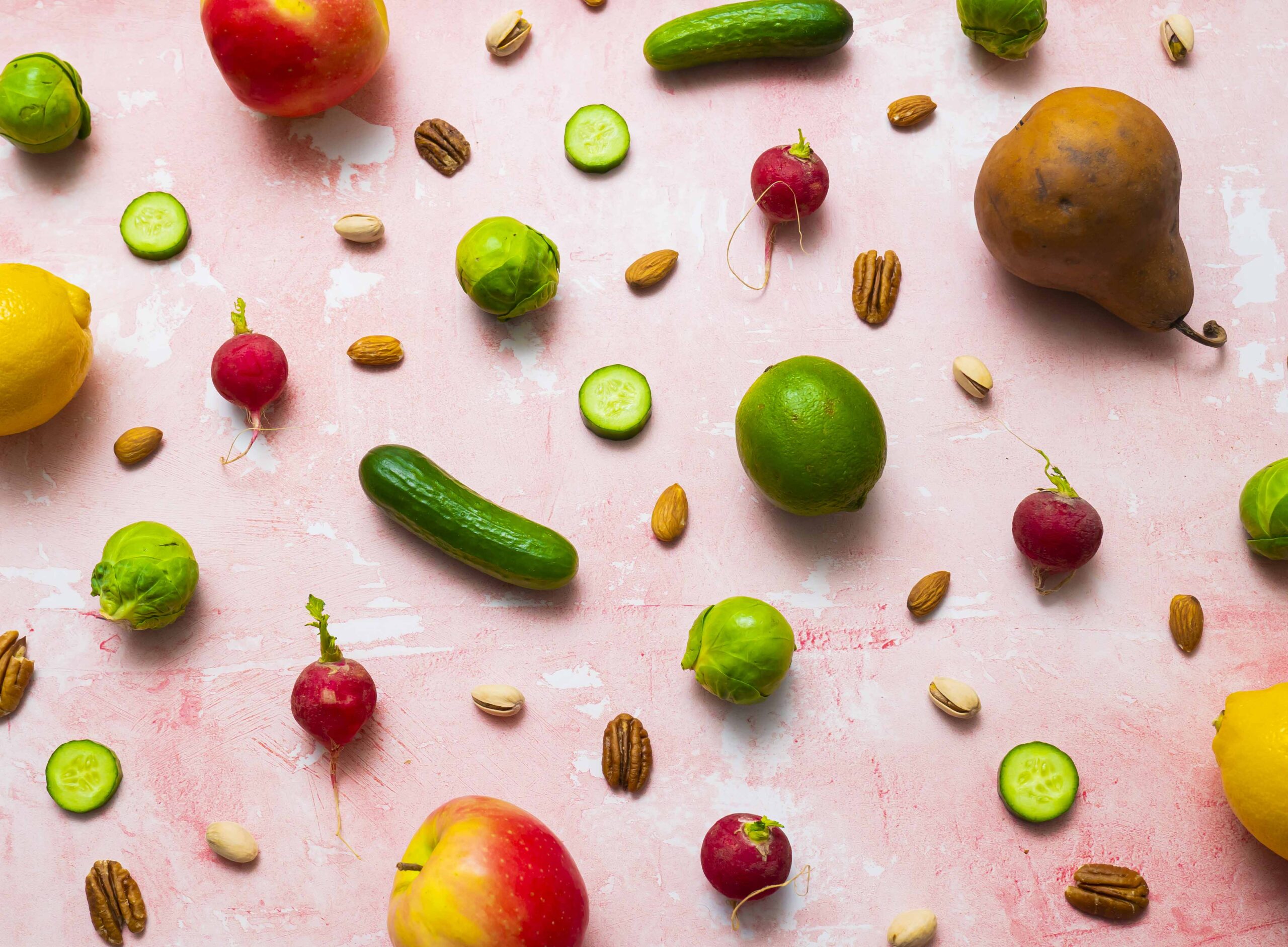 A variety of fruits, vegetables and nuts against a pink background.