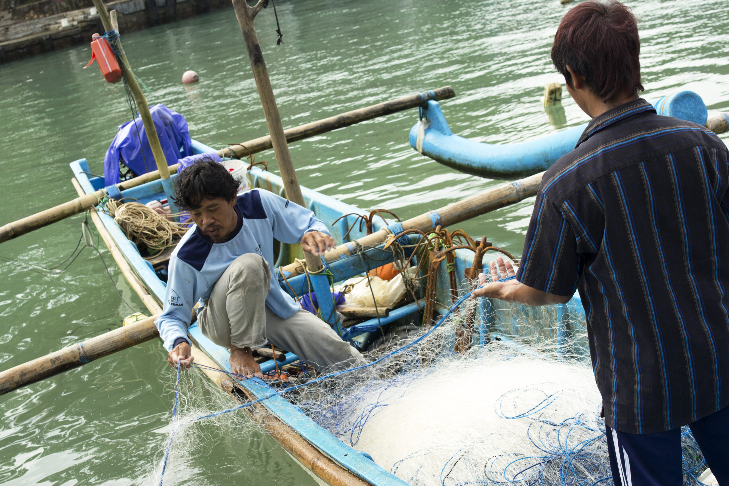 Two men on a boat untangling fish gear.