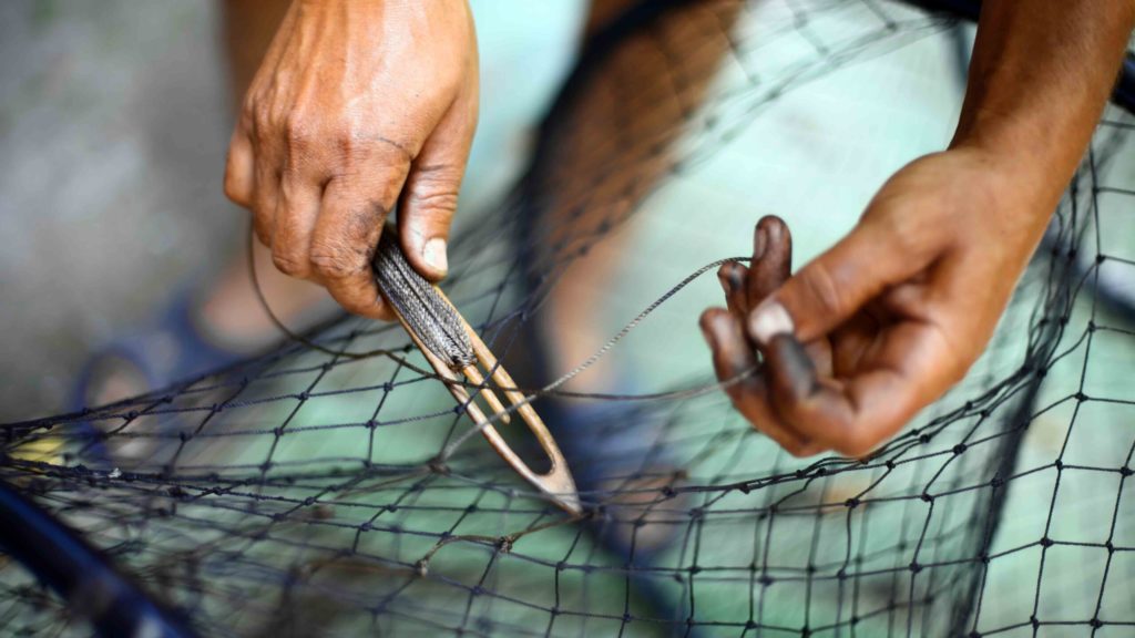 Color detail of a man repairing a fishing net.