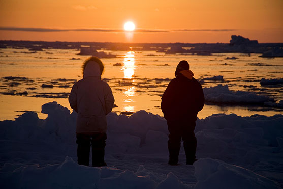Silhouette of Inupiaq subsistence whalers at the edge of an open lead in the pack ice, looking for passing bowhead whales as the mid-day sun follows the horizon. Chukchi Sea, offshore from Barrow, Arctic coast of Alaska, May 2012.